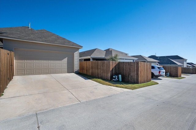 view of side of property featuring a residential view, concrete driveway, roof with shingles, and fence