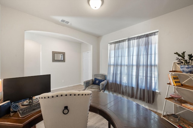 office with arched walkways, visible vents, baseboards, and wood finished floors