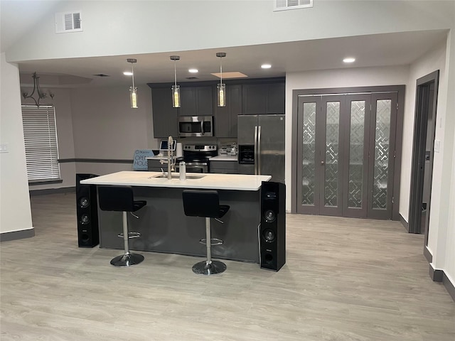 kitchen featuring a kitchen bar, a center island with sink, stainless steel appliances, and decorative light fixtures