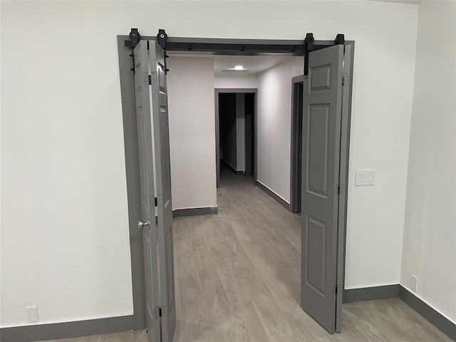 hallway with a barn door and light hardwood / wood-style floors