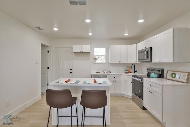 kitchen featuring white cabinetry, light hardwood / wood-style flooring, a breakfast bar, a kitchen island, and appliances with stainless steel finishes