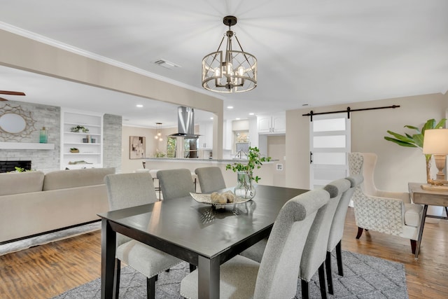 dining area with a large fireplace, a barn door, built in features, hardwood / wood-style flooring, and ornamental molding