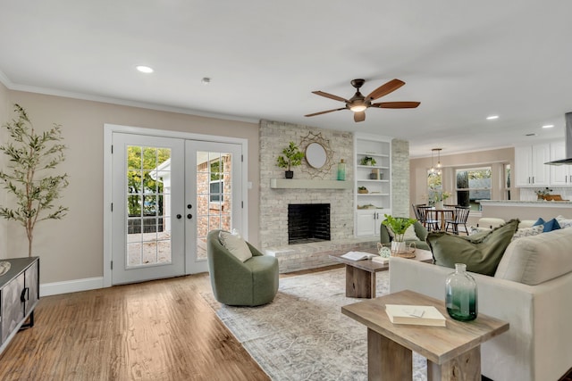 living room with crown molding, a brick fireplace, built in shelves, french doors, and light wood-type flooring