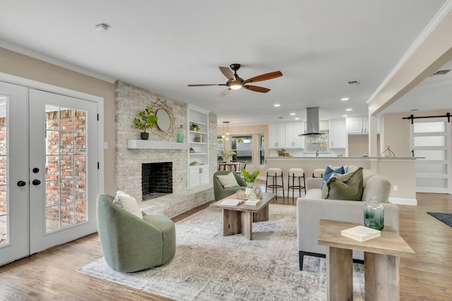 living room with a barn door, light hardwood / wood-style flooring, ceiling fan, and crown molding