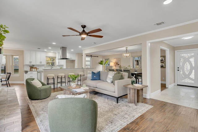 living room with a barn door, crown molding, ceiling fan with notable chandelier, and light wood-type flooring