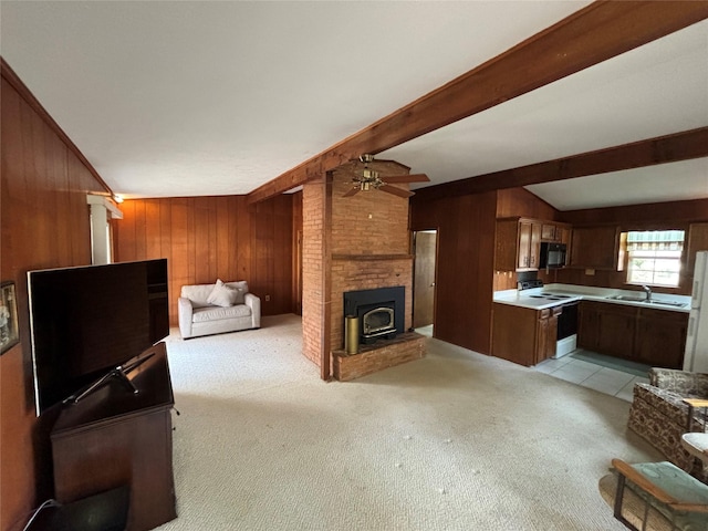 living room featuring a wood stove, light carpet, sink, wooden walls, and ceiling fan