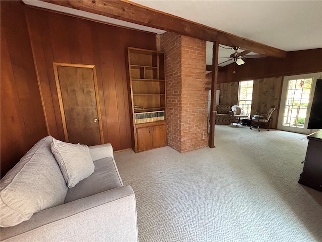 carpeted living room with wooden walls, beamed ceiling, and ceiling fan