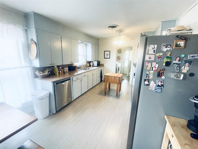 kitchen featuring appliances with stainless steel finishes, light wood-type flooring, separate washer and dryer, and sink