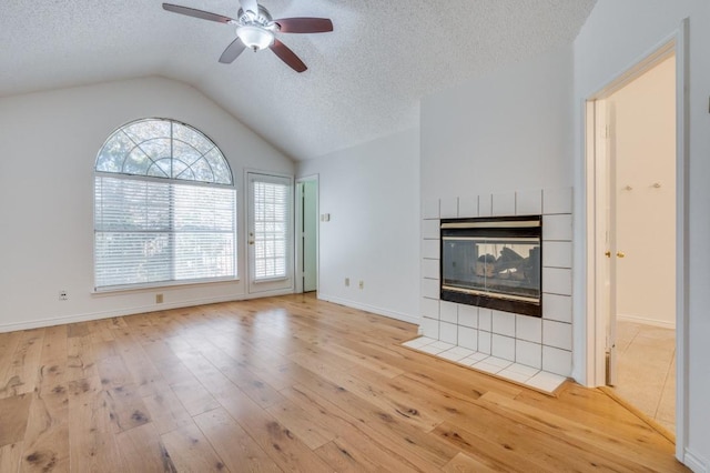 unfurnished living room featuring ceiling fan, light hardwood / wood-style flooring, a textured ceiling, lofted ceiling, and a tiled fireplace