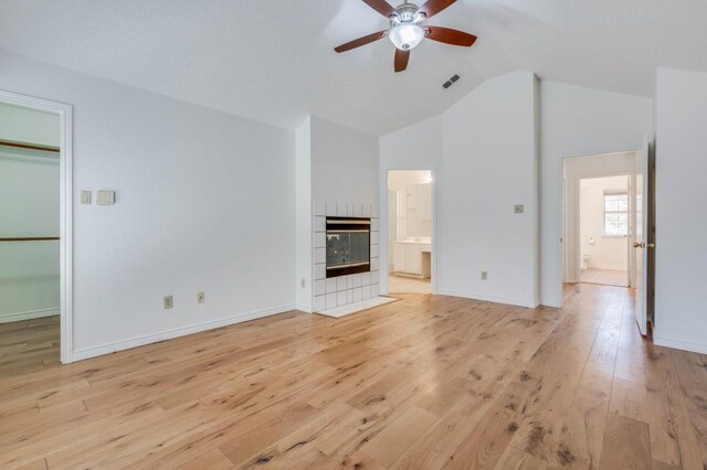 unfurnished living room featuring a tiled fireplace, ceiling fan, high vaulted ceiling, and light wood-type flooring