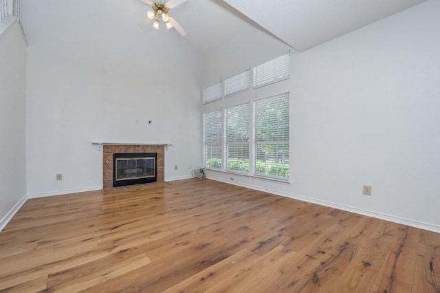 unfurnished living room featuring ceiling fan, light hardwood / wood-style floors, high vaulted ceiling, and a tiled fireplace