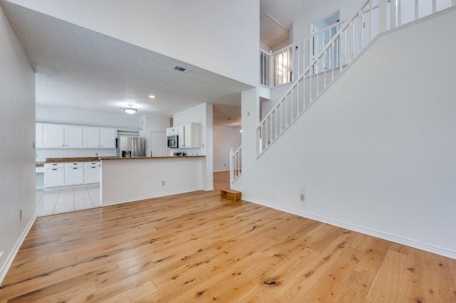 unfurnished living room with a high ceiling, a textured ceiling, and light hardwood / wood-style flooring