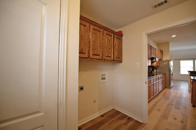 clothes washing area with hookup for an electric dryer, washer hookup, light hardwood / wood-style floors, and cabinets