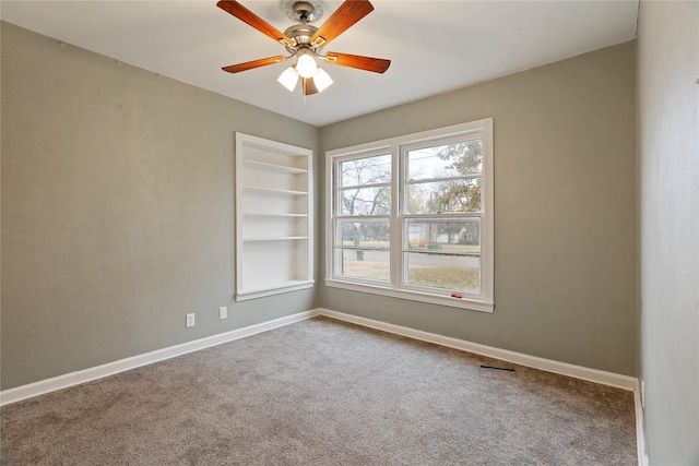 unfurnished room featuring carpet flooring, built in shelves, and ceiling fan