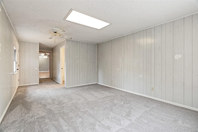 spare room featuring carpet flooring, ceiling fan, a textured ceiling, and wooden walls