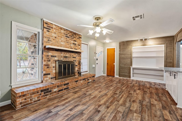 unfurnished living room with ceiling fan, a fireplace, and dark wood-type flooring