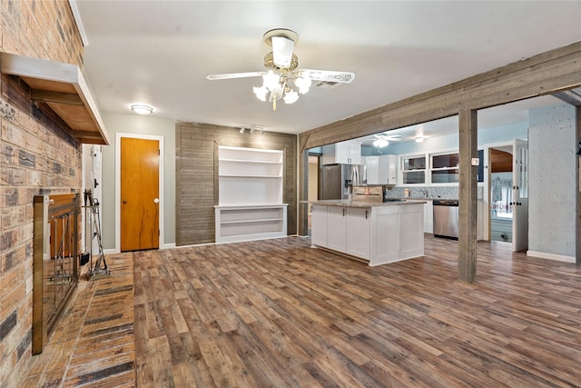 kitchen featuring white cabinets, stainless steel appliances, wooden walls, and dark wood-type flooring