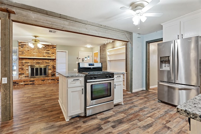 kitchen with white cabinets, light stone countertops, appliances with stainless steel finishes, wood-type flooring, and brick wall