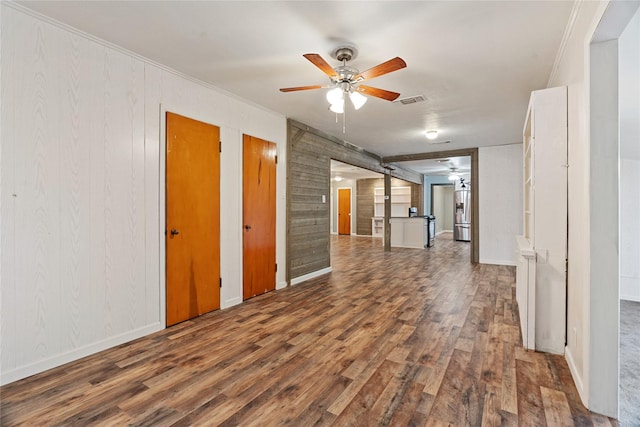 empty room featuring crown molding, ceiling fan, dark wood-type flooring, and wood walls