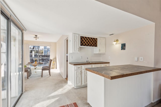 kitchen featuring white cabinetry, sink, kitchen peninsula, and light carpet