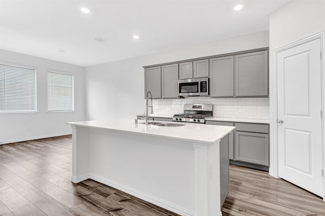 kitchen with sink, decorative backsplash, stainless steel appliances, and a center island with sink