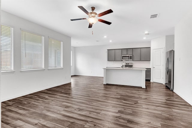 kitchen featuring appliances with stainless steel finishes, dark hardwood / wood-style flooring, tasteful backsplash, ceiling fan, and a center island with sink