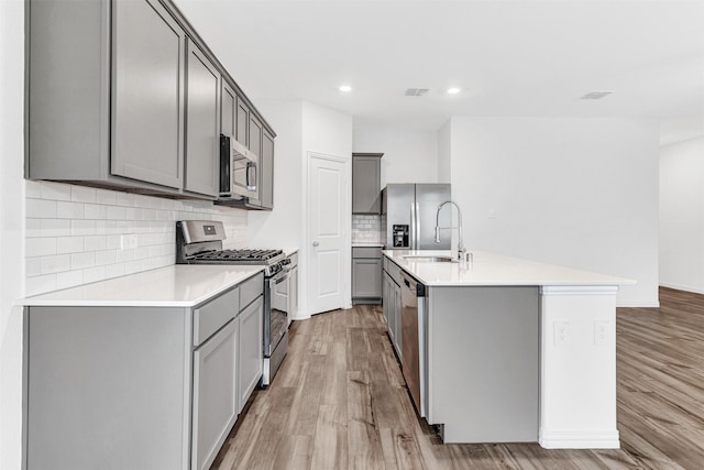 kitchen with gray cabinets, light hardwood / wood-style flooring, an island with sink, and stainless steel appliances