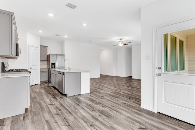 kitchen with light hardwood / wood-style floors, stainless steel appliances, a kitchen island with sink, ceiling fan, and gray cabinets