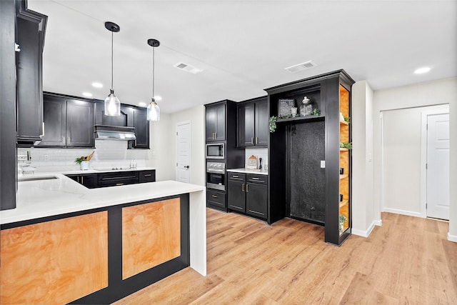 kitchen with light wood-type flooring, black electric cooktop, built in microwave, sink, and decorative light fixtures