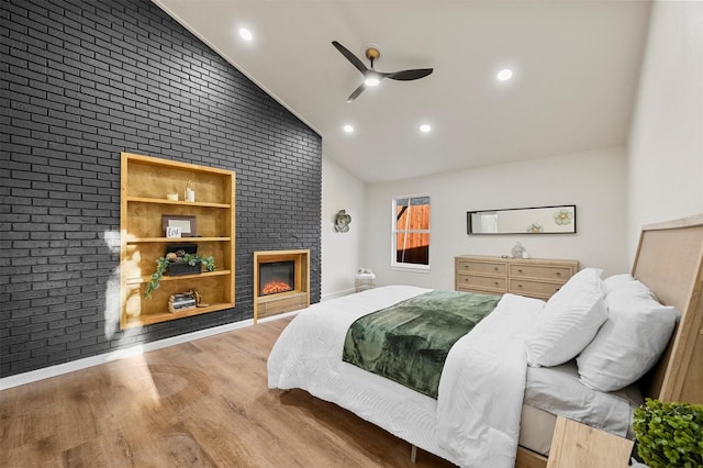 bedroom with ceiling fan, brick wall, wood-type flooring, vaulted ceiling, and a fireplace