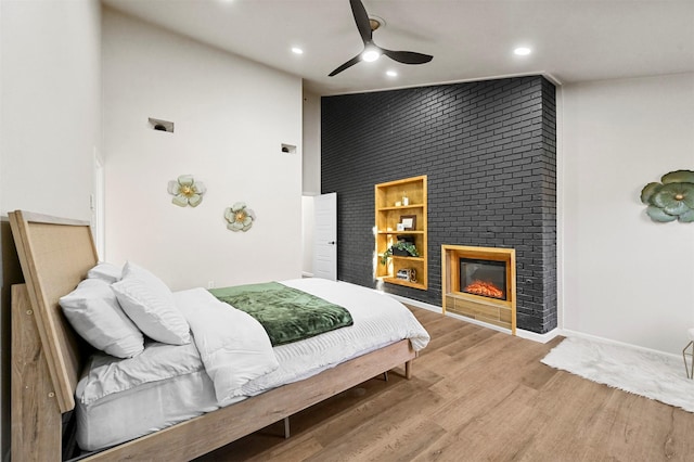 bedroom featuring a fireplace, hardwood / wood-style floors, a towering ceiling, and ceiling fan