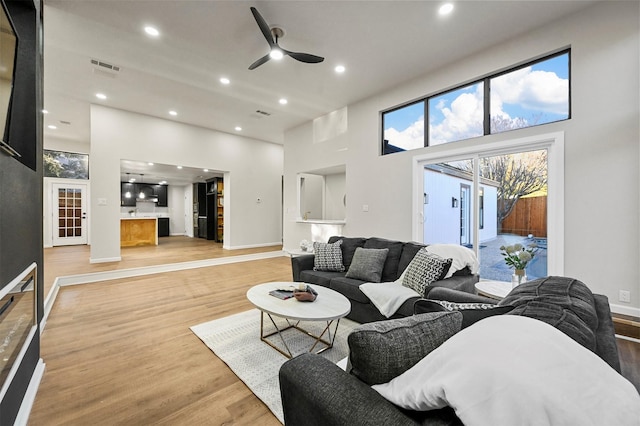 living room with a towering ceiling, light hardwood / wood-style floors, and ceiling fan