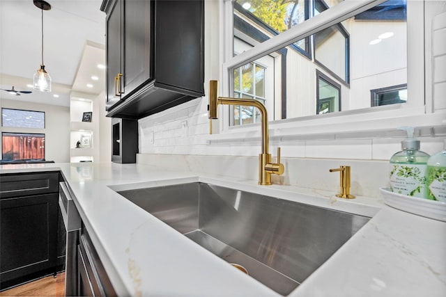 kitchen featuring backsplash, light stone counters, sink, and hanging light fixtures