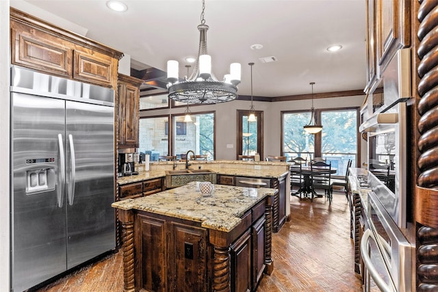 kitchen with built in fridge, pendant lighting, sink, a center island, and dark brown cabinets