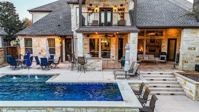 back of property with a balcony, an outdoor bar, a fireplace, a fenced in pool, and a patio