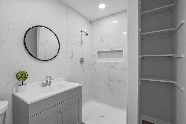 bathroom with vanity, toilet, and tiled shower