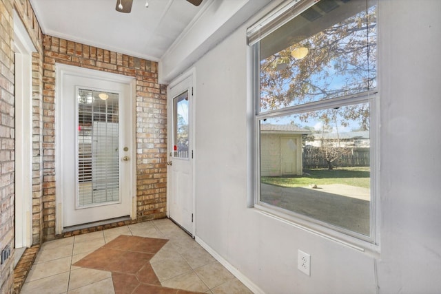 doorway featuring crown molding, light tile patterned floors, brick wall, and ceiling fan