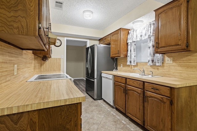 kitchen with decorative backsplash, a textured ceiling, white appliances, sink, and light tile patterned floors