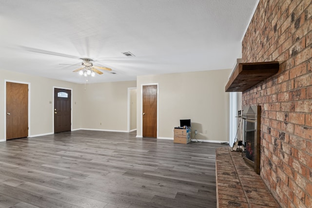 unfurnished living room with a fireplace, ceiling fan, dark wood-type flooring, and brick wall