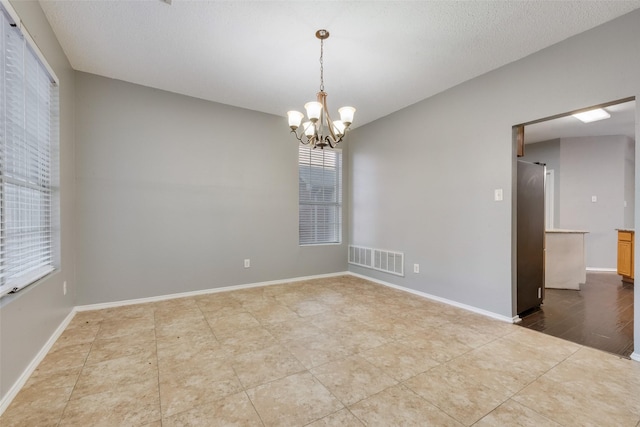 tiled spare room featuring an inviting chandelier, a wealth of natural light, and a textured ceiling