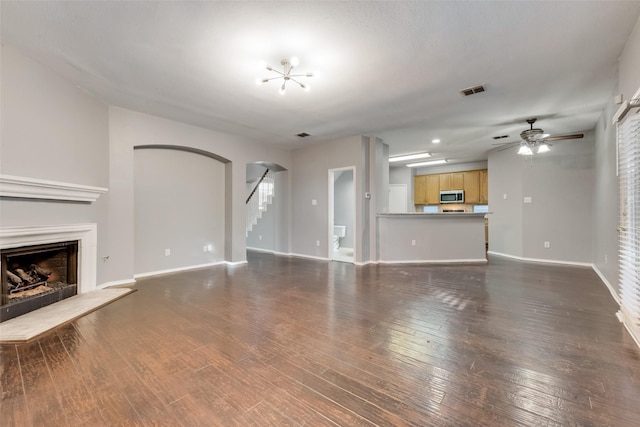 unfurnished living room with ceiling fan with notable chandelier and dark wood-type flooring