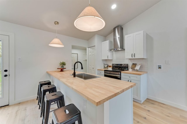 kitchen featuring kitchen peninsula, wall chimney exhaust hood, stainless steel electric stove, sink, and white cabinets