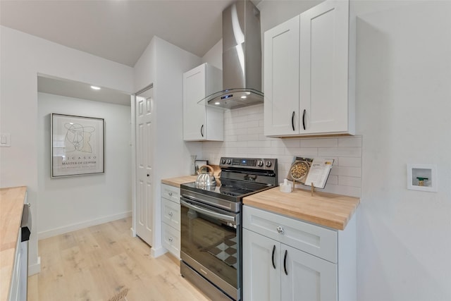 kitchen with wood counters, stainless steel electric stove, wall chimney range hood, light hardwood / wood-style floors, and white cabinetry