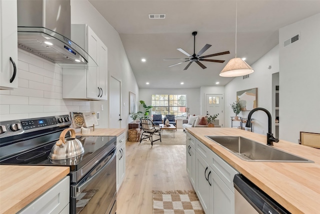 kitchen featuring hanging light fixtures, wall chimney exhaust hood, butcher block countertops, white cabinetry, and stainless steel appliances