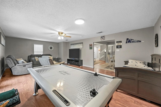 rec room with ceiling fan, a textured ceiling, and light wood-type flooring