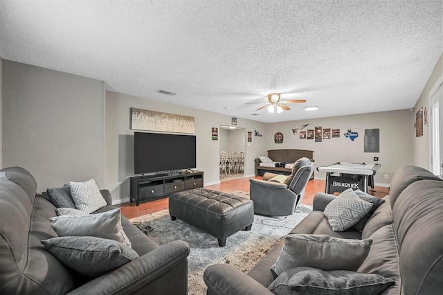 living room featuring ceiling fan, a textured ceiling, electric panel, and hardwood / wood-style floors