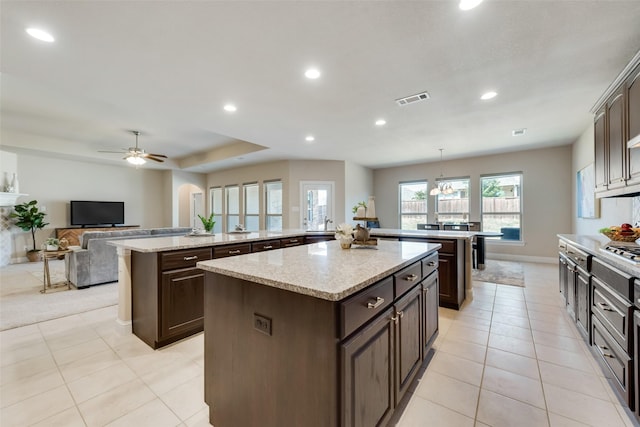 kitchen with ceiling fan with notable chandelier, hanging light fixtures, light tile patterned floors, dark brown cabinets, and a kitchen island