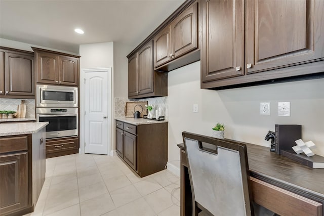 kitchen with stainless steel appliances, light tile patterned floors, dark brown cabinets, and backsplash