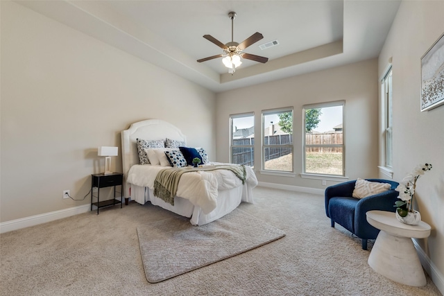 carpeted bedroom with ceiling fan and a tray ceiling