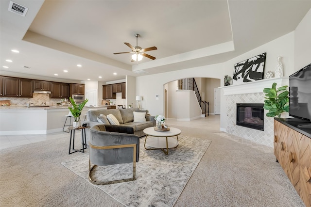 living room with a tiled fireplace, a raised ceiling, and light carpet